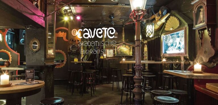 The interior of the Cavete Bar is furnished with wooden tables, stools and decorative mirrors, which are illuminated by soft lighting and create a cozy atmosphere.