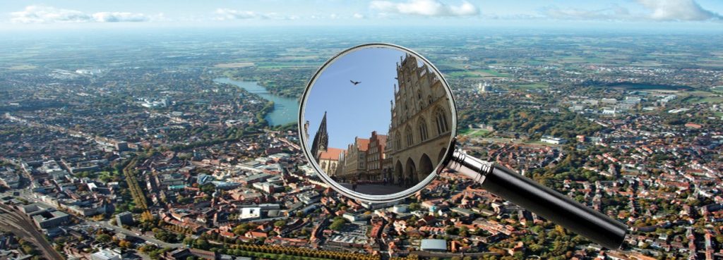 Eine Stadt in der Vogelperspektive mit einer Lupe, welche einen Teil vergrößert